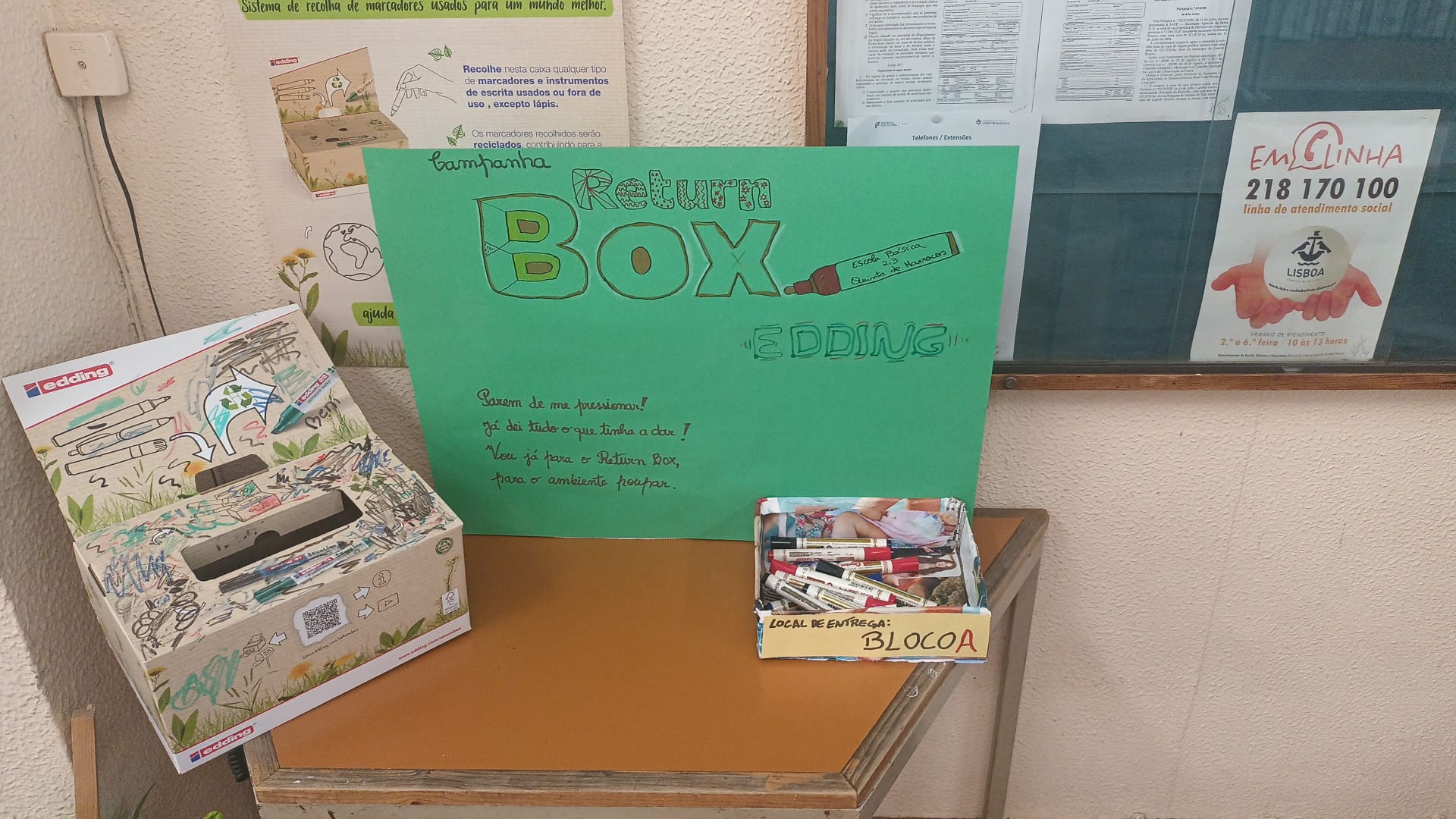 Retur box posicionada na entrada do Bloco A, tendo ao lado o cartaz da Return Box feito pelos alunos, que tem uma estrutura para se manter na vertical.