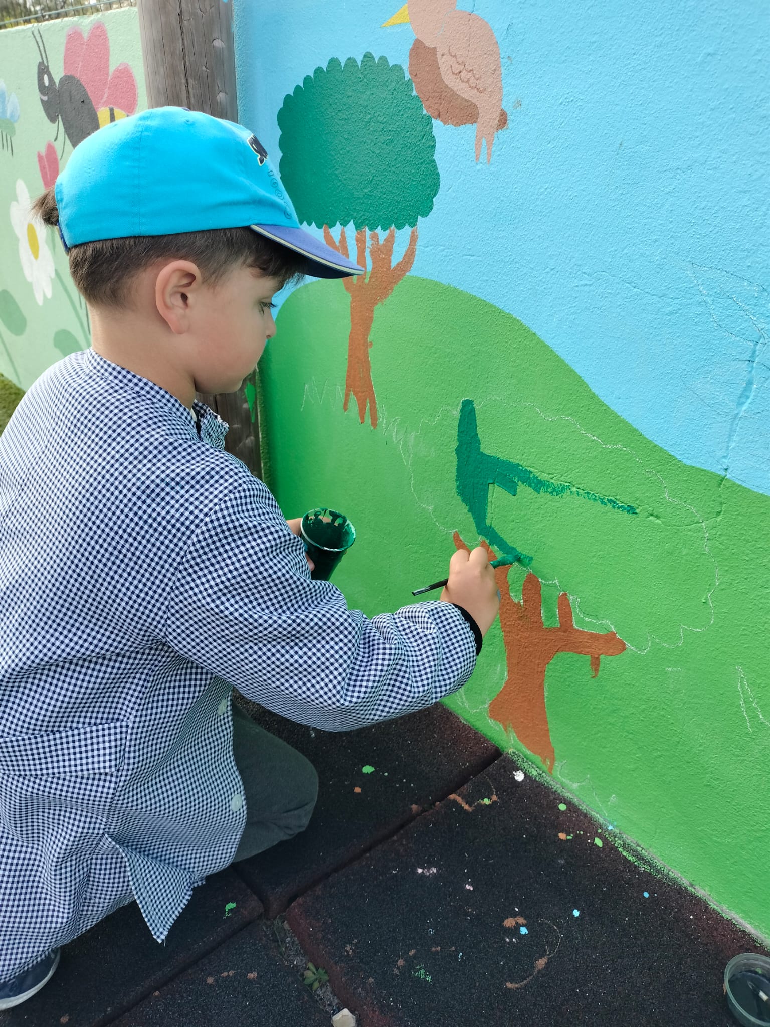 Criança a pintar uma das árvores presentes no muro e que faz parte da biodiversidade da região.
